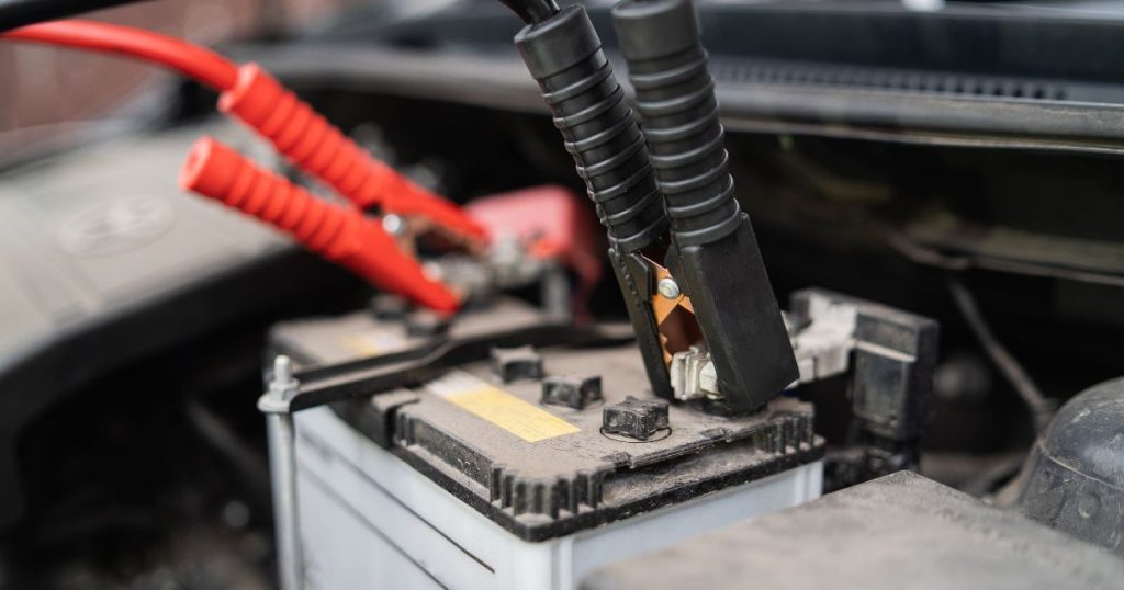 Detailbeeld van een loodzuurbatterij van een oude auto. Een rode en een zwarte startkabel zijn aangesloten op de batterij.