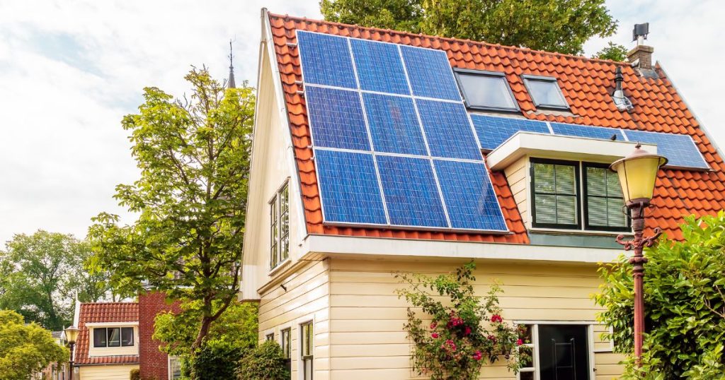 Een woning met rood pannendak, witte houten gevel, dakkapel, dakramen, schouw en zonnepanelen in een groene buurt.