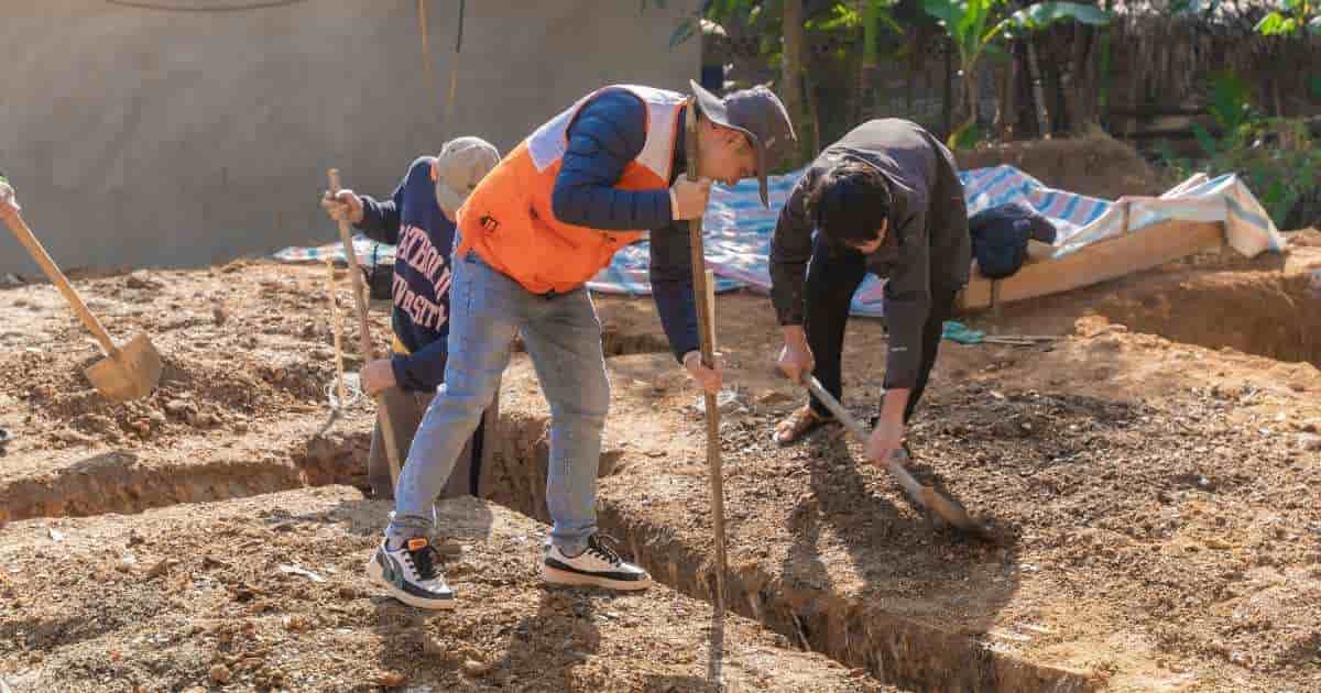 Drie mannen in werkkledij zijn bezig met de uitzetwerken als voorbereiding op de graafwerken voor het aanleggen van een zwembad. Ze gebruiken spades.