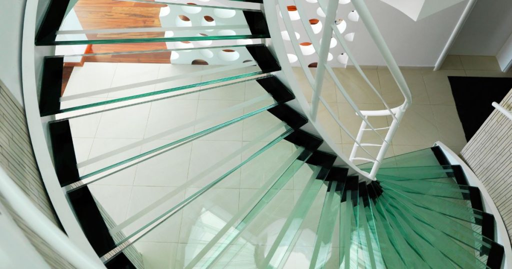 Een stalen wenteltrap met glazen treden en witte balustrade.