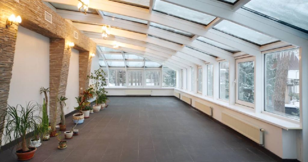 Een veranda aanbouw met steellook aluminium profielen die doorlopen in het glazen dak en een zwarte tegelvloer.