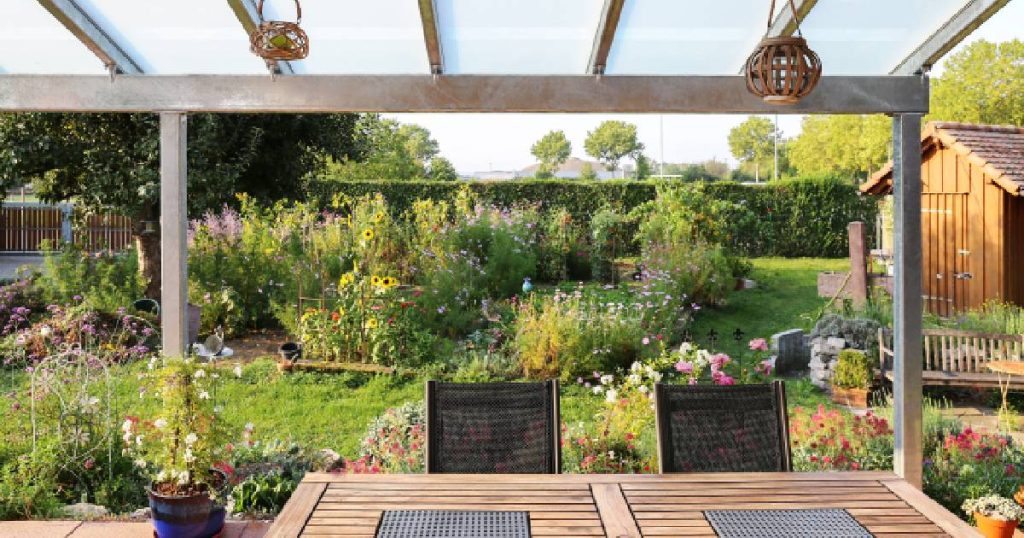 Een moderne steellook veranda zonder zijwanden met uitzicht op een groene tuin.