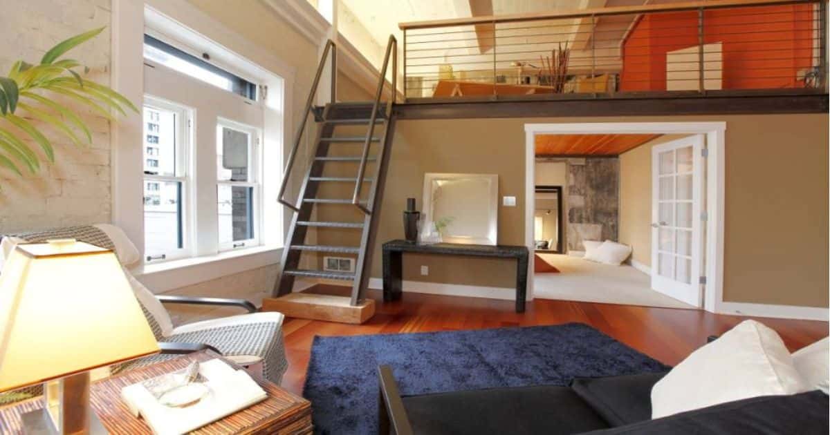 Metalen steile trap in woonkamer, naast een wit raam.