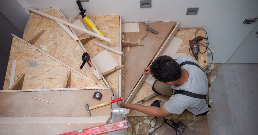 Een trappenbouwer plaatst een stootbord tegen een traptrede. Hij gaat daarbij heel secuur te werk, gebruikmakend van diverse tools of gereedschap.