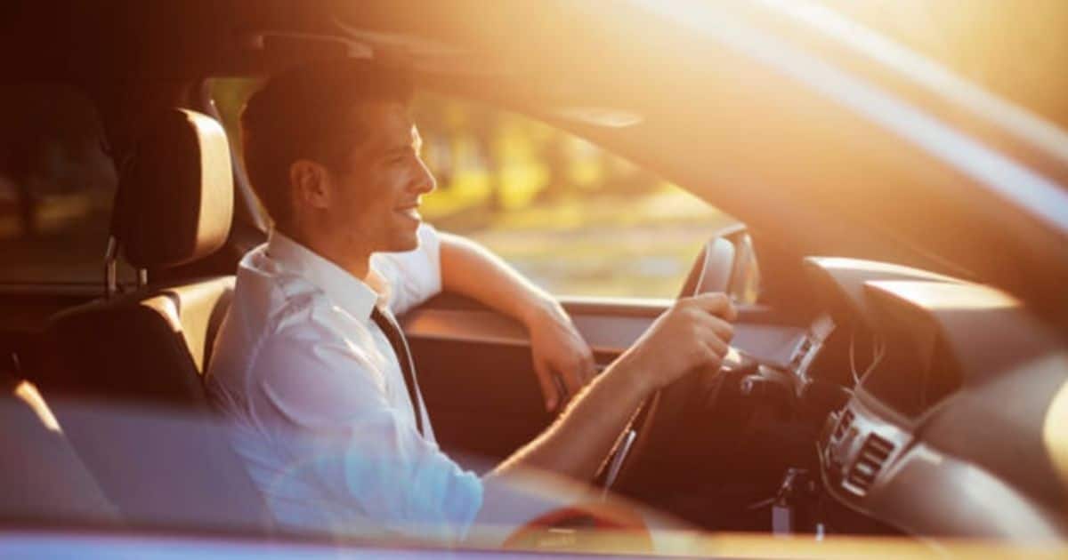 Bestuurder achter het stuur van een auto met zonlicht dat door de voorruit valt.