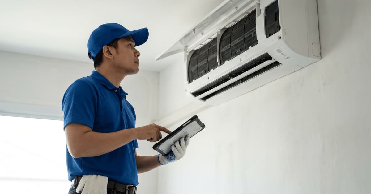 Een technicus in blauw poloshirt kijkt omhoog naar een geopende witte airco-binnenunit met zichtbare filters terwijl hij een tablet in zijn hand houdt.