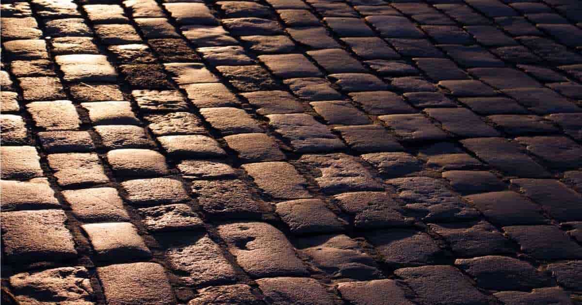 Grijze kasseien weerspiegelen warmgeel licht.