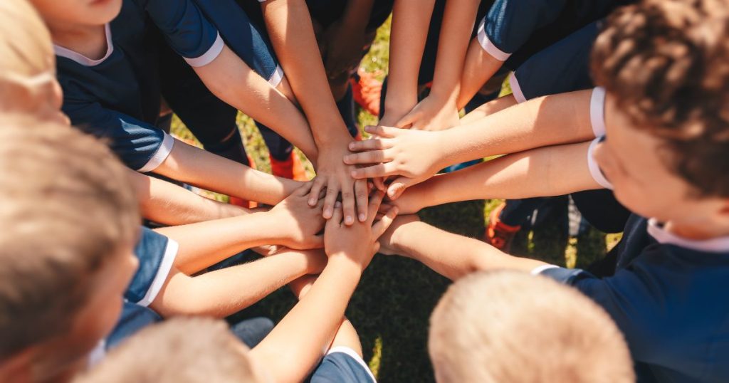 Een groep kinderen in sporttenues houdt de handen op elkaar in een grote kring.