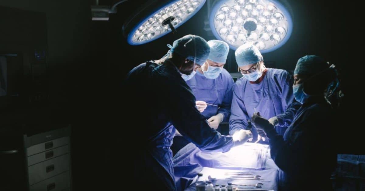 Vier artsen rond een patiënt in een operatiekamer met grote ronde lampen.