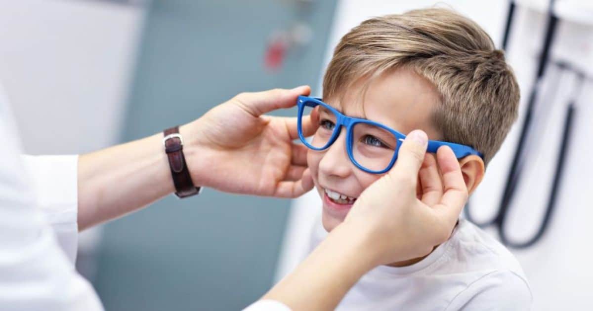 Een jongen krijgt een blauw brilmontuur aangemeten door 2 handen.