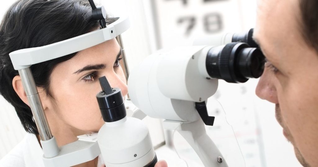 Een oogarts controleert de iris en de oogsterkte van een vrouwelijke patiënte met een speciaal toestel. De oogarts kijkt door 2 bijzondere lenzen, terwijl de patiënte zelf voor zich uitstaart.