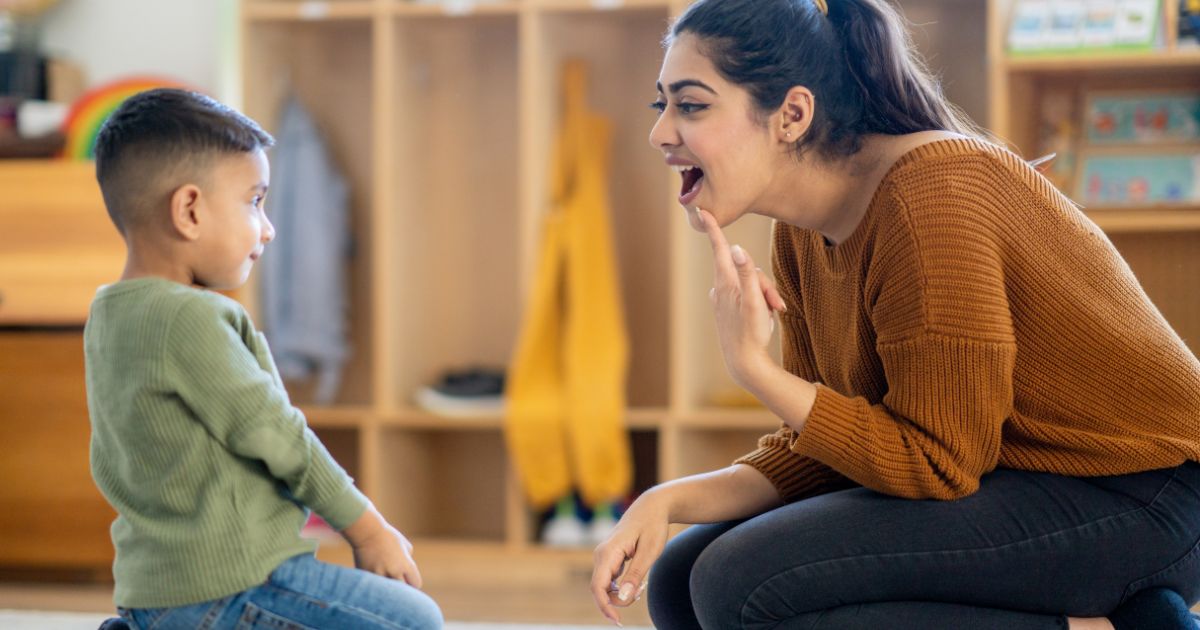 Een logopedist wijst naar haar mond om haar jonge patiënt te helpen met zijn spraakprobleem.