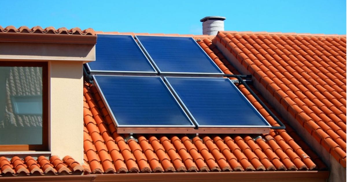 Op een roodbruin dak liggen vier thermische zonnepanelen. De lucht is erg helder en blauw