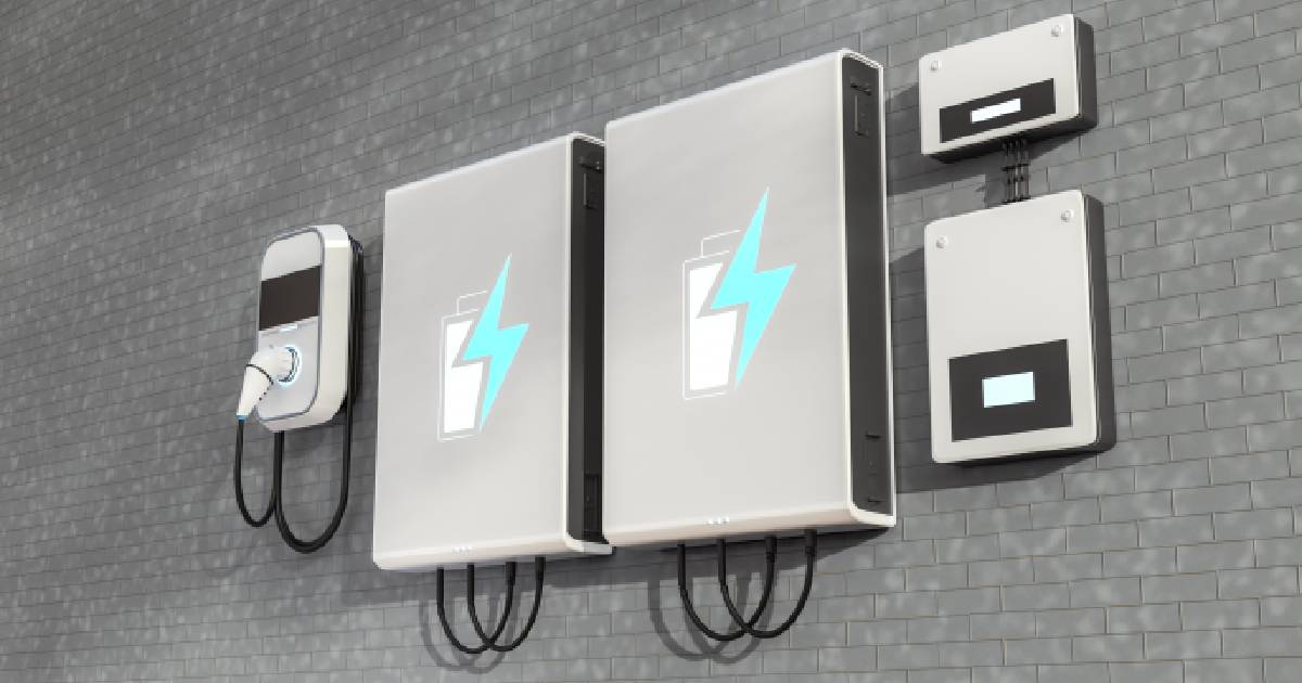 Een thuisbatterij, wallbox laadpaal en omvormers tegen een grijze, bakstenen gevel: een systeem met een vrij hoge prijs, maar een goede oplossing voor wie zoveel mogelijk van de zelfopgewekte zonne-energie wilt verbruiken.