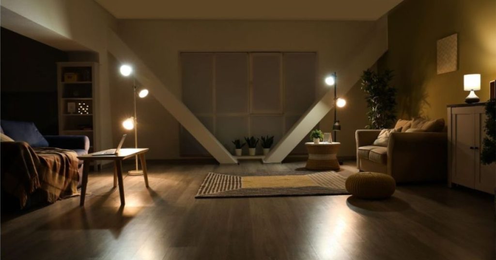 Een living 's avonds met lichtspots op een staander als sfeerverlichting. Dankzij een thuisbatterij kan je de overdag opgeslagen zonne-energie als het donker wordt benutten voor onder meer je verlichting.
