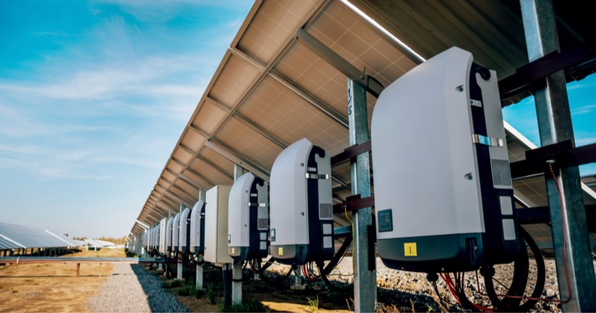 Een rij witte thuisbatterijen die onder een rij zonnepanelen staan
