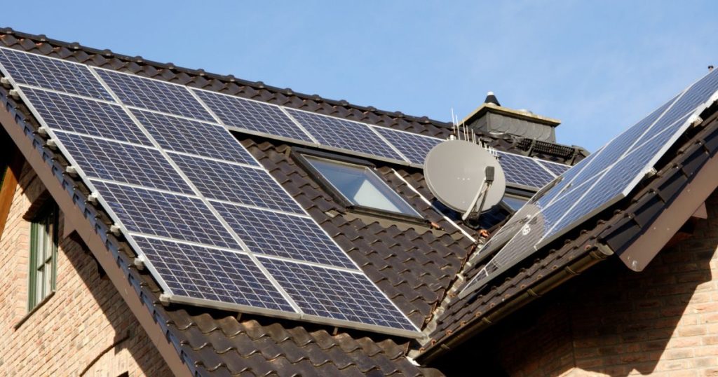 Een schuin dak met zwarte dakpannen, een zonnepaneelinstallatie, dakramen, schouw en satelliet. 
