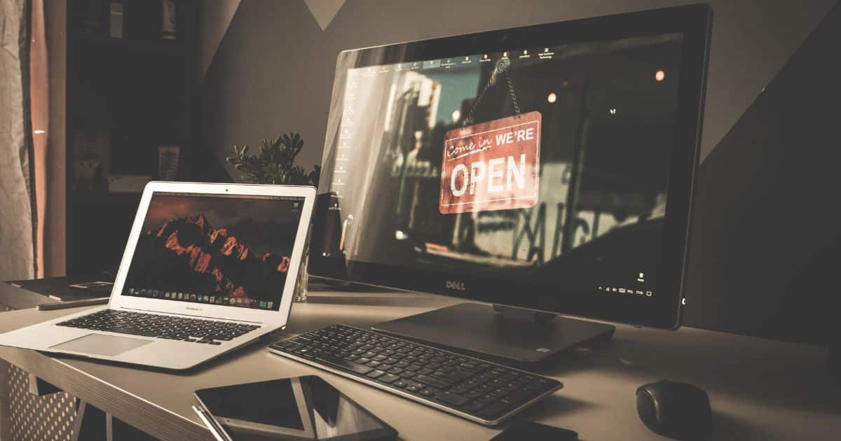 Een kleine laptop of notebook naast een groot computerscherm met apart toetsenbord en muis. Op de tafel waarop de 2 computers staan, ligt ook een zwarte tablet.
