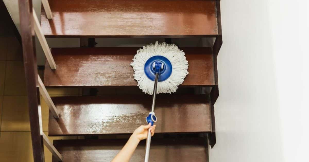 Een trap met houten trapbekleding: een goed alternatief op vinyl, maar wel een minder onderhoudsvriendelijke optie. Een dame gebruikt een dweil om de houten trap te onderhouden.
