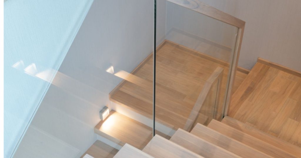 Een trap na een renovatie: houten traptreden en een glazen balustrade met metalen trapleuning.