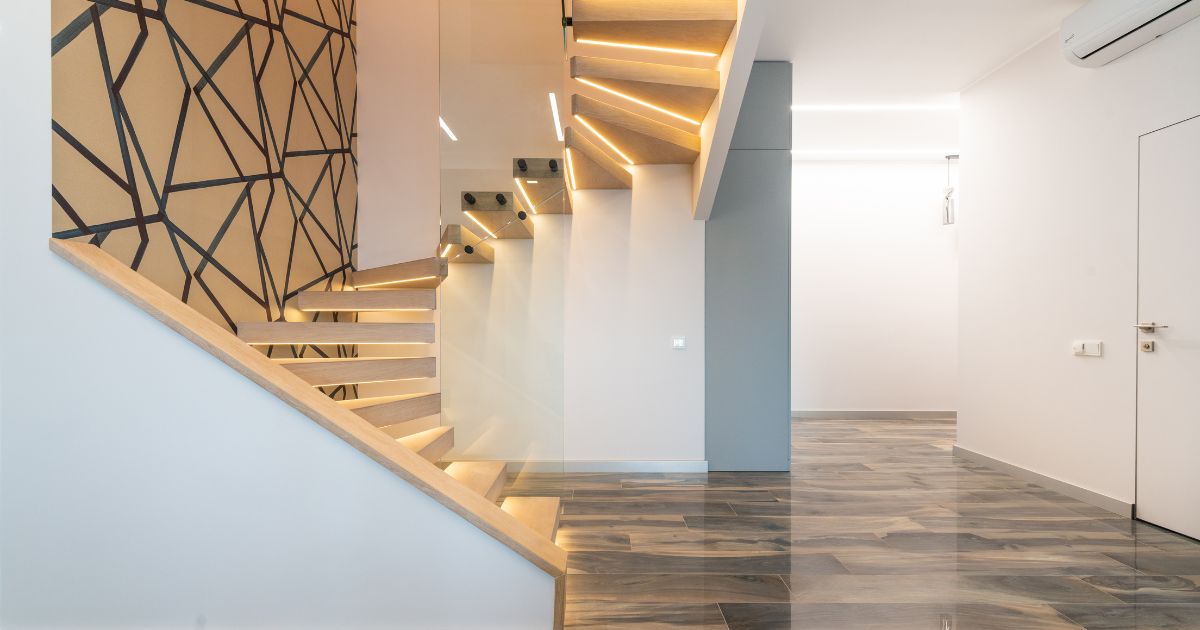 Zwevende trap in hout met verlichting onder elke traptrede in strak en minimalistisch interieur. Waar de trap een bocht maakt is een extra glazen wand voorzien.