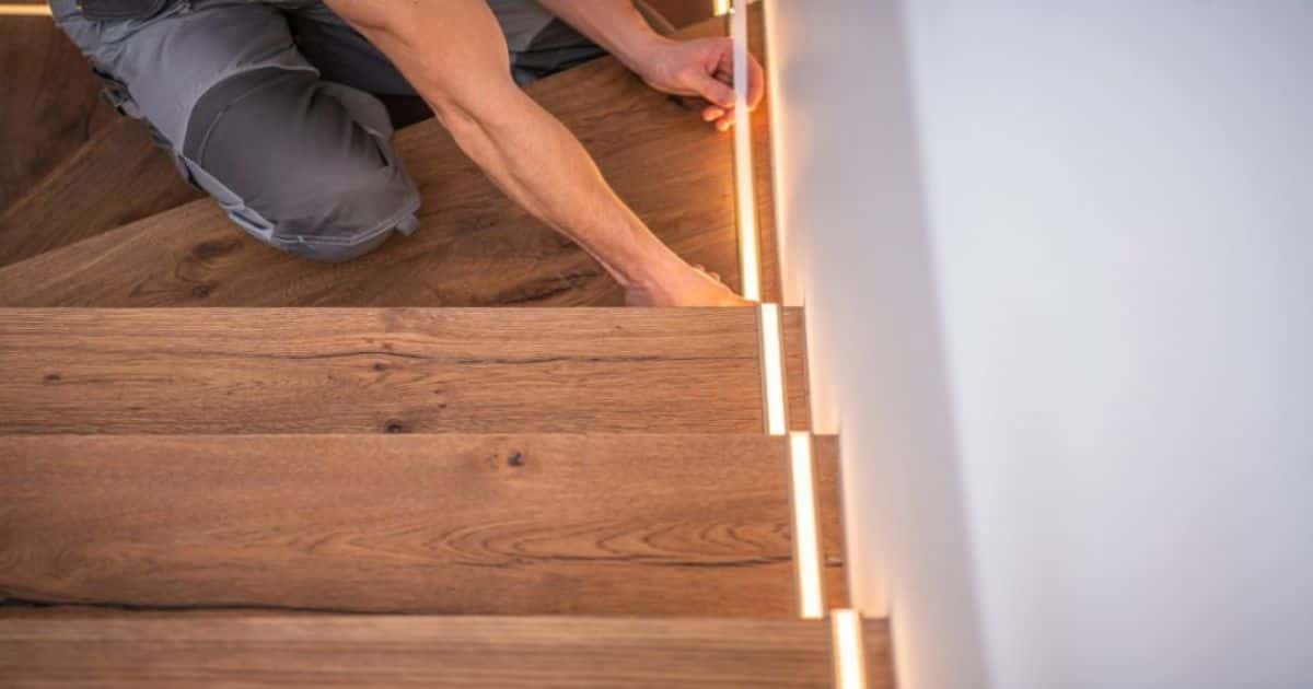 Trap wordt gerenoveerd in woning. Een werkman voorziet ledverlichting langs de zijkant van de trap.