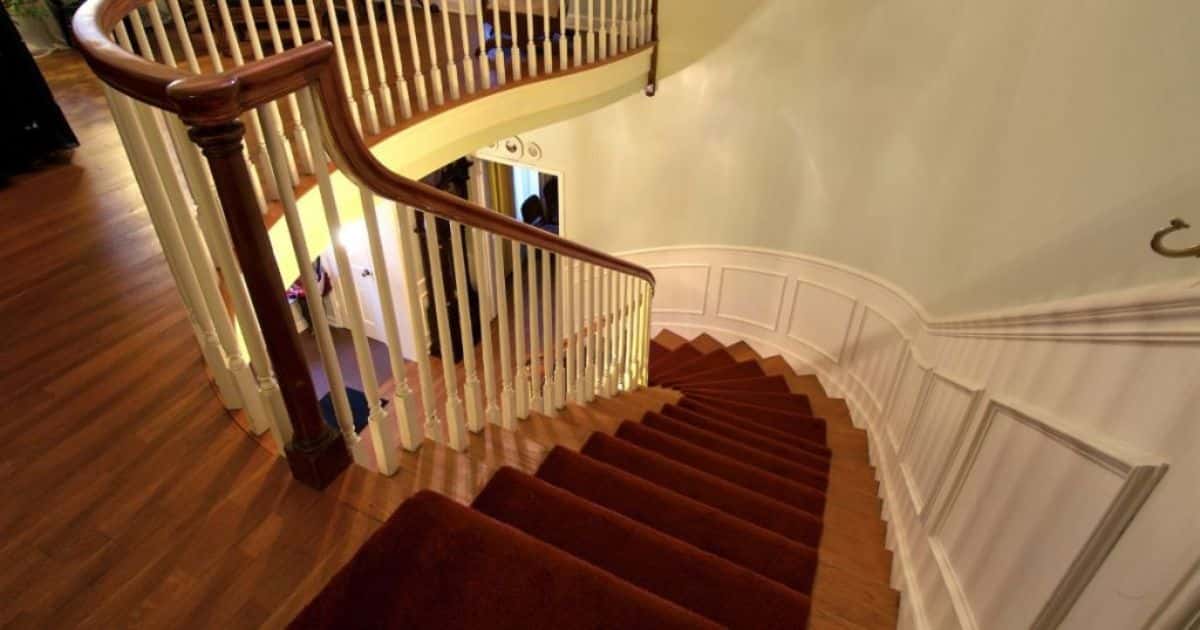 Het trapgat met traphek van een houten trap met rood tapijt.