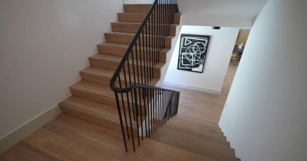 Dit is een houten trappengat met zwarte leuning. 