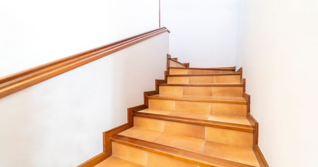 Een trap in een witte trappenhal, afgewerkt met tegels, houten trapwangen, houten trapneuzen en een houten trapleuning.