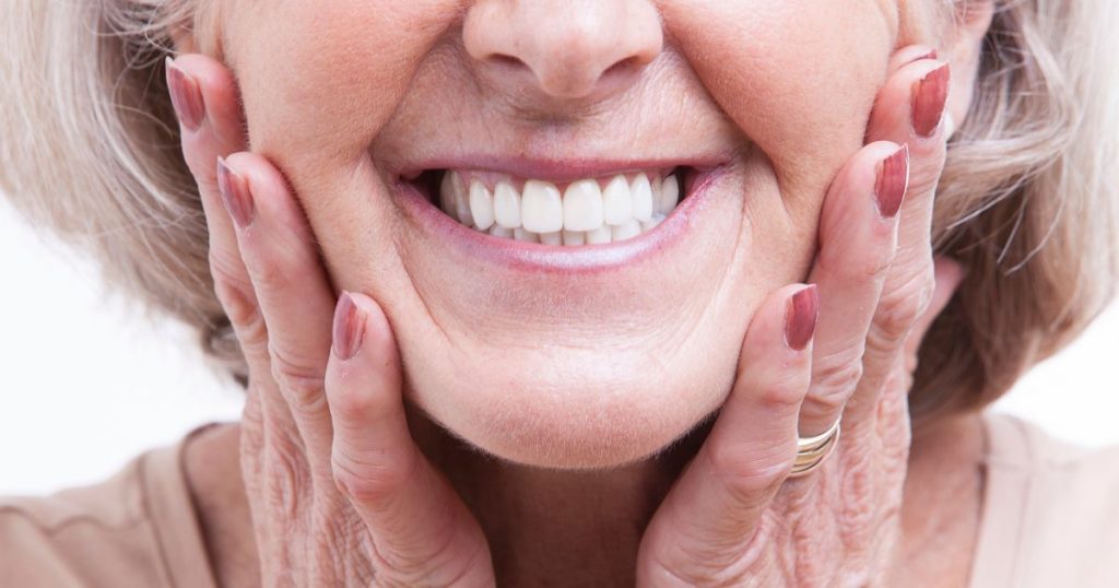 Close-up van de onderste helft van het gezicht van een vrouw met kort haar. Ze houdt twee handen op haar kaken.