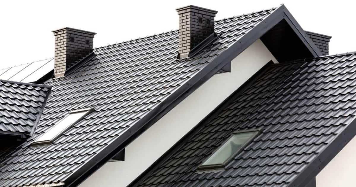 Een wit huis met twee schoorstenen en een zwart grijs dak.
