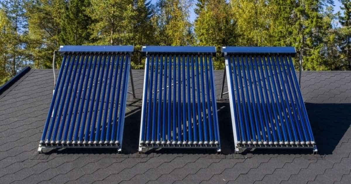 Drie sets met blauwe zonnecollectoren op een zwart hellend dak. Enkele grote bomen steken uit boven het dak.