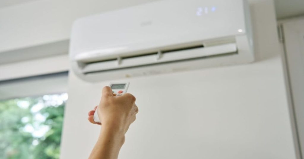 Een hand houdt een afstandsbediening van een vaste airco vast en zet de airco op 21 graden