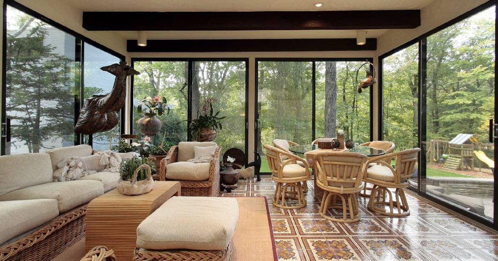 Een veranda met goede isolatie, verwarming en ventilatie. In de droge, warme veranda staan verschillende meubels, planten en decoratiestukken. De glazen wanden zonder condens geven uit op een ruime, groene tuin.