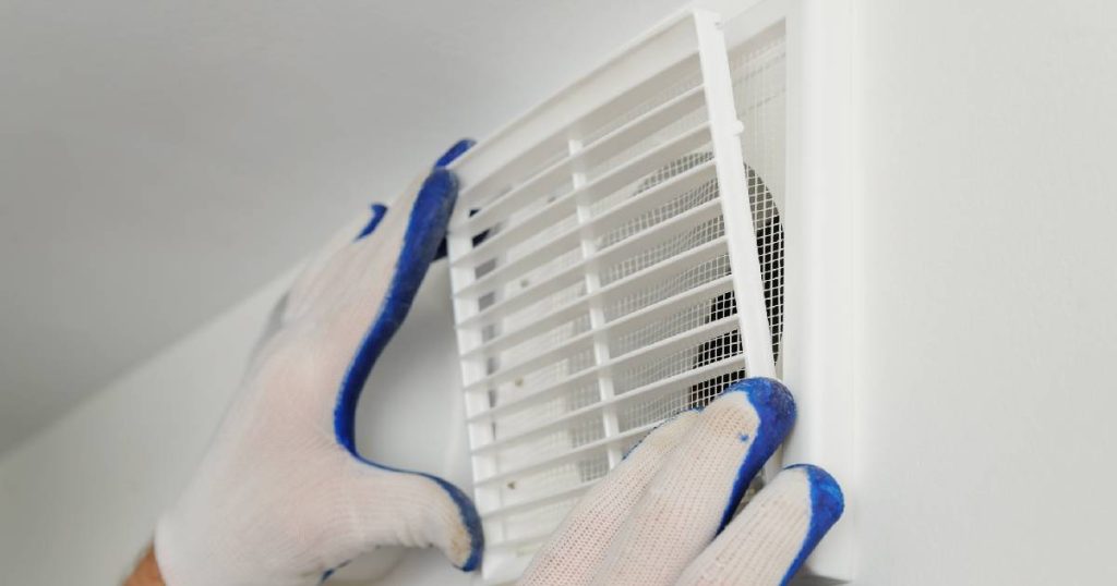Twee handen in wit met blauwe werkhandschoenen monteren een ventilatierooster in een veranda.