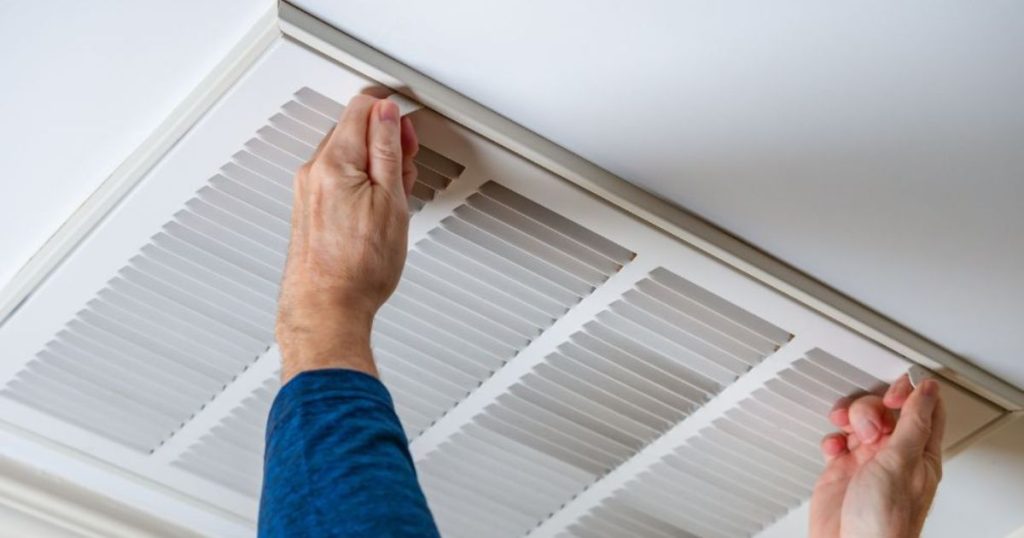 Persoon die een ventilatierooster in het plafond opent.