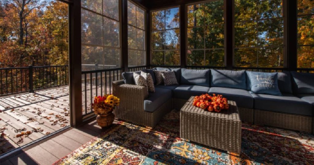 Een gezellige veranda die men heeft laten dichtmaken met glas. Het glas zit in grote houten frames. De veranda beschikt over een glazen schuifdeur die uitgeeft op een onbedekt terras. In de veranda staat een grote rieten zetels met donkere, blauwgrijze kussens en een rieten bijzettafeltje. Onder de zetel ligt een tapijt.