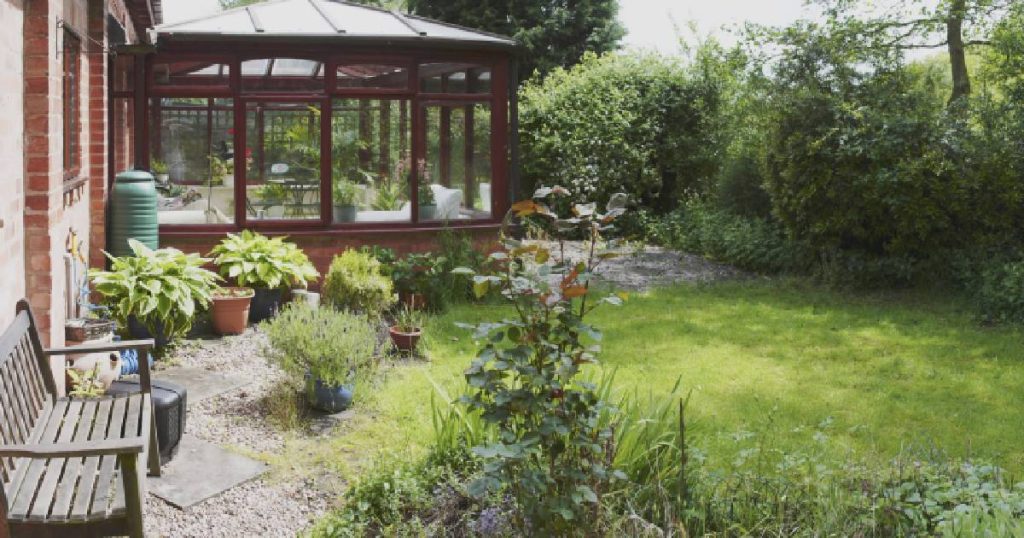 Vooraanzicht met een tuin met veranda. Men heeft de veranda laten dichtmaken met hout en grote ramen. 