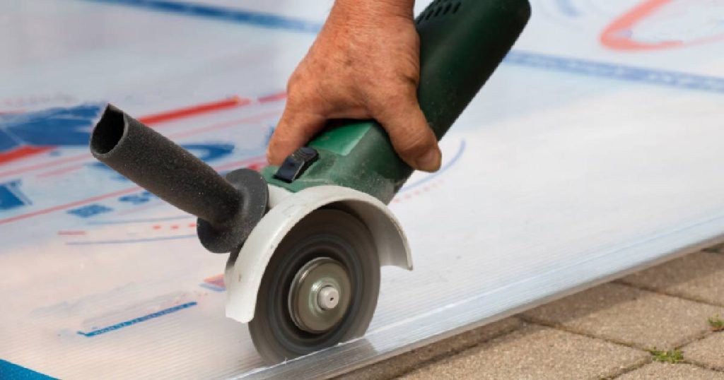 Een man gebruikt een cirkelzaag met fijne tanden en groen handvat om plexiglas op maat te snijden waarmee hij zijn veranda dichtmaken zal. De plexiglasplaat wordt volledig ondersteund door een harde ondergrond met tegels.