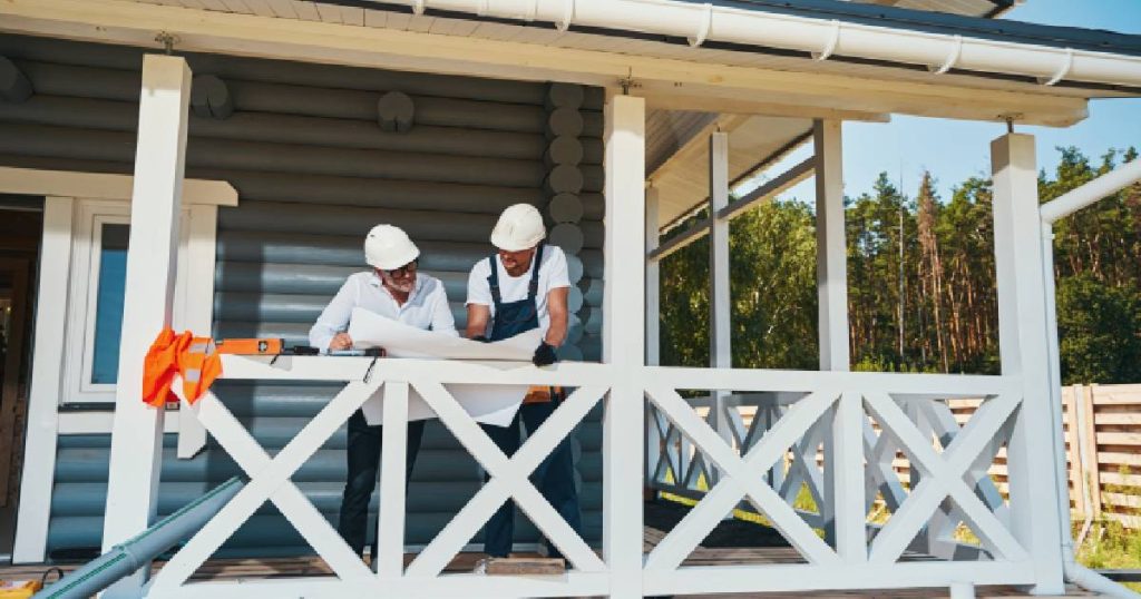 Twee mannen met witte veiligheidshelmen die zelf een veranda aan het maken zijn bestuderen een bouwtekening.