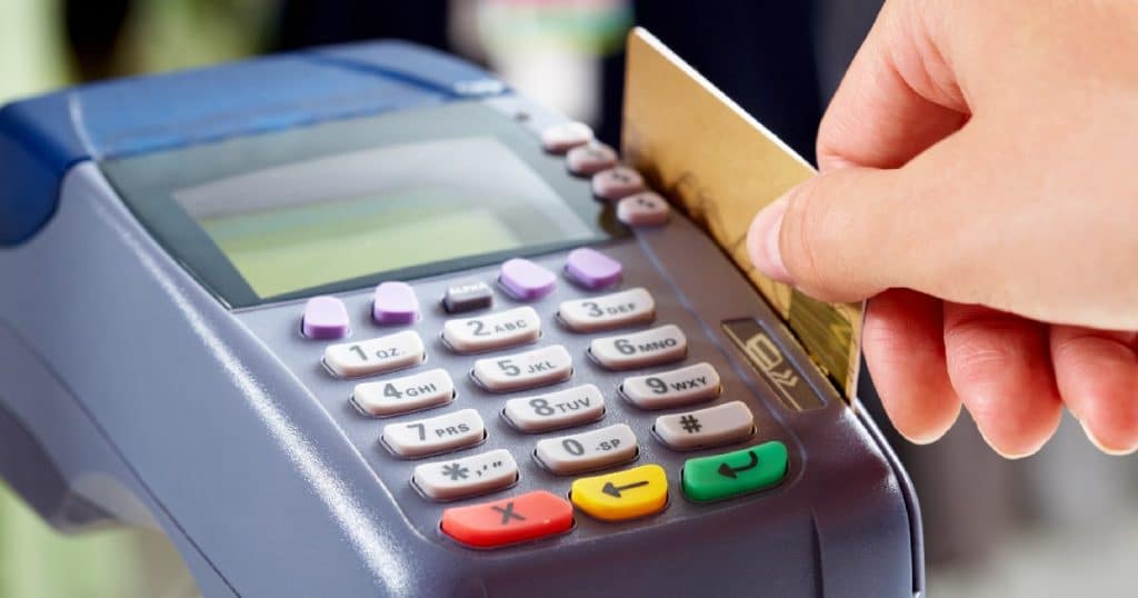 Een dame stopt haar kredietkaart in de gleuf van een donkergrijze betaalterminal die ook debetkaarten aanvaardt.