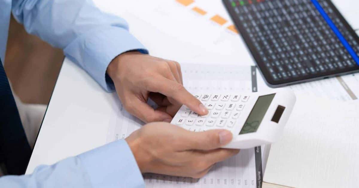 Een werknemer bij een sociaal secretariaat doet de loonadministratie voor een bedrijf. Hij gebruikt papieren met tabellen, een tablet en een rekenmachine.