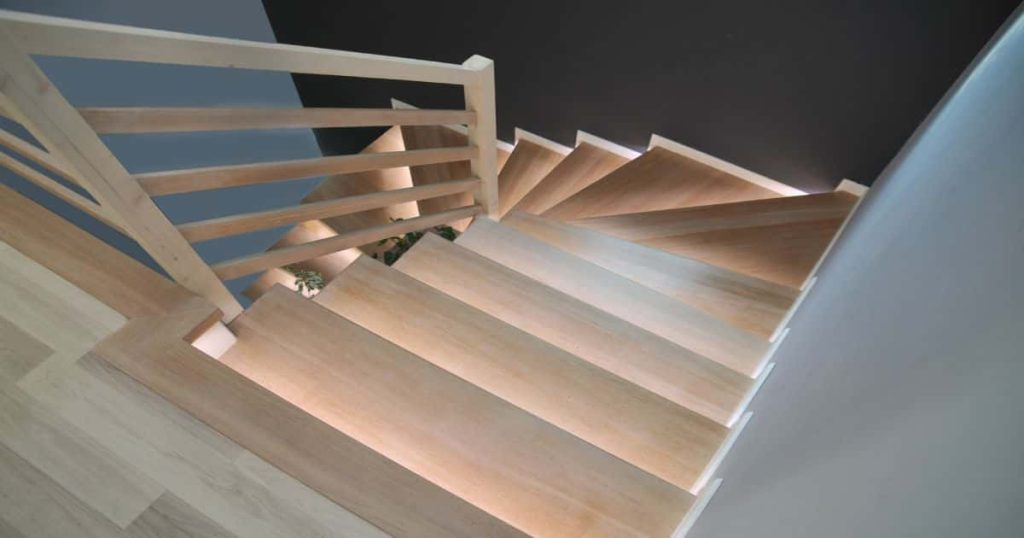 Een steile trap met overzettreden in vinyl in lichte houtlook. De trapverlichting maakt het gebruik van de trap veiliger in de donkere ruimte.