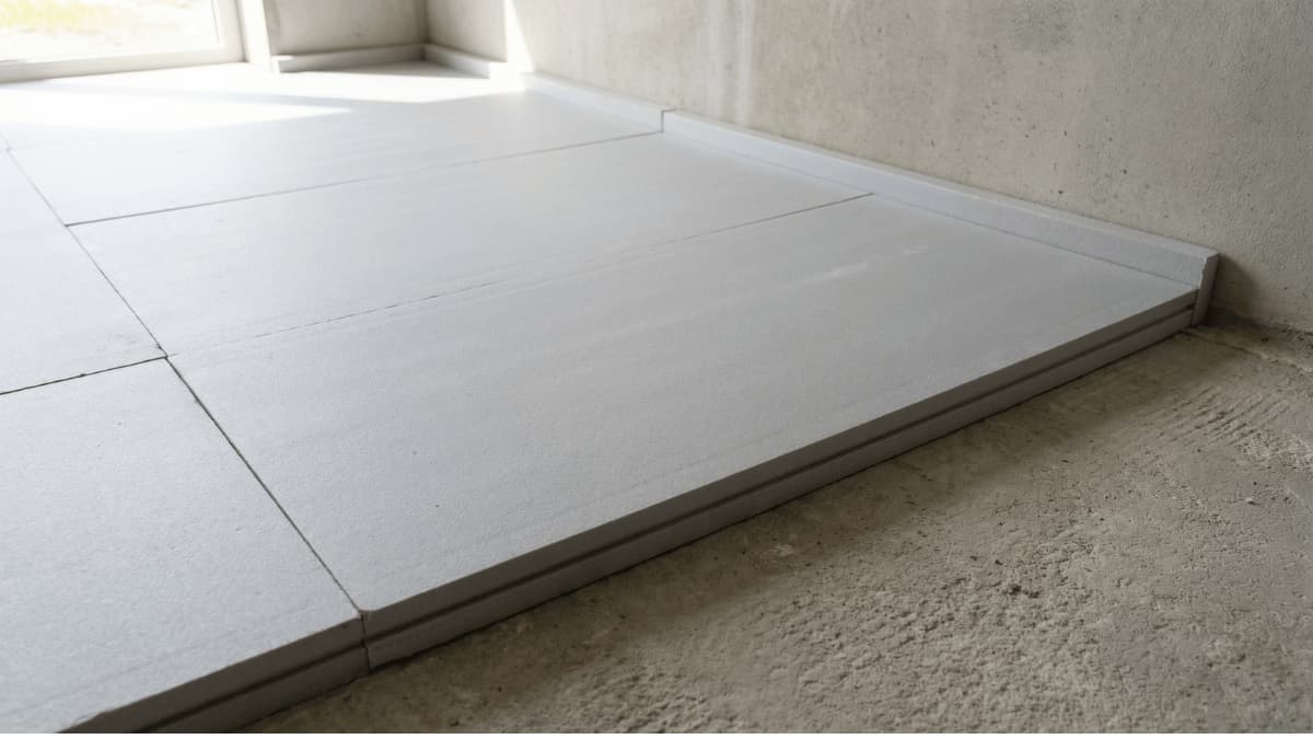 Rigide isolatieplaten netjes gelegd op een betonvloer met zichtbare randstrook langs de muur voor vloerisolatie langs de bovenzijde.