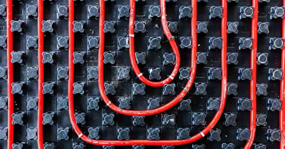 Bovenaanzicht van rode buizen voor vloerverwarming tussen zwarte kunststof noppen.