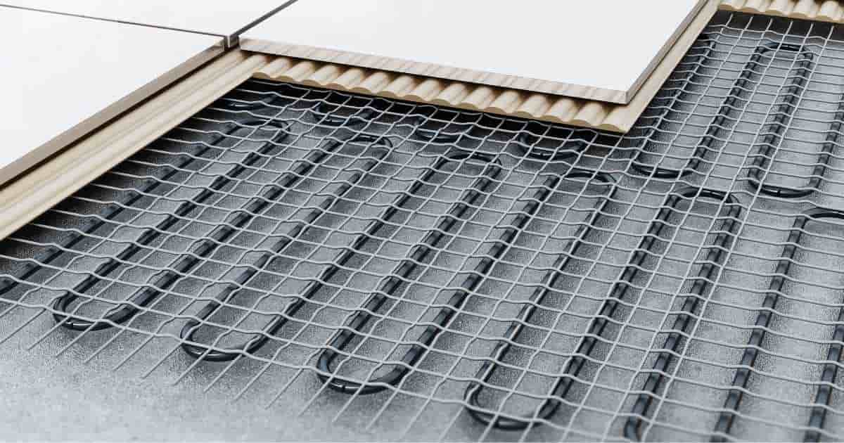 Verschillende lagen in een verwarmde vloer: de zwarte verwarmingsbuizen, een metalen raster, de ondervloer en de witte tegels die de vloerafwerking vormen.