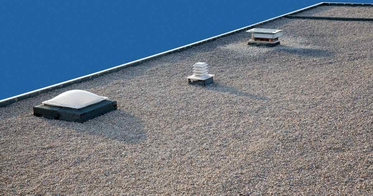 Een plat dak bedekt met een laag EPDM en een ballastlaag van grind. In het dak zitten een klein dakraam en twee openingen voor een ventilatiesysteem.