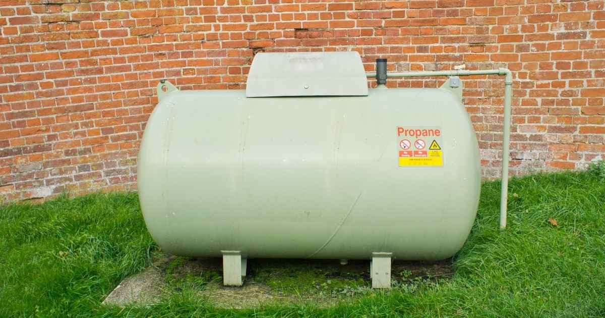 Een lichtgroene gastank tegen een bakstenen scheidingsmuur. De tank is via een ondergrondse leiding verbonden met de woning.