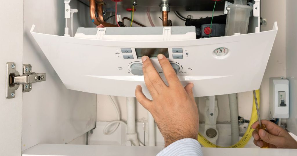 Twee handen bij een klassieke gasboiler: de ene hand opent het voorpaneel, de andere hand gebruikt gereedschap om aan de boiler te sleutelen.