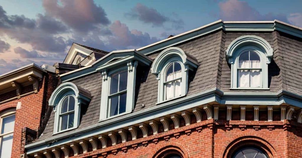 Detail van een statig gebouw met klassiek mansardedak, afgewerkt met lichtblauw geverfde houten dakkapellen met kruishouten.